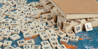 Foto: Auf kleinen Holztäfelchen bedruckte Buchstaben liegen durcheinander in einem Buch und quillen hier heraus, so dass auch einige auf dem Boden liegen.