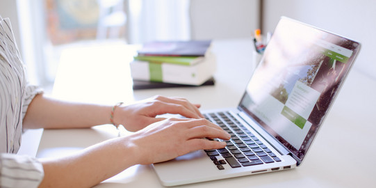 Studentin tippend am Laptop, daneben liegen Bücher und Stifte.